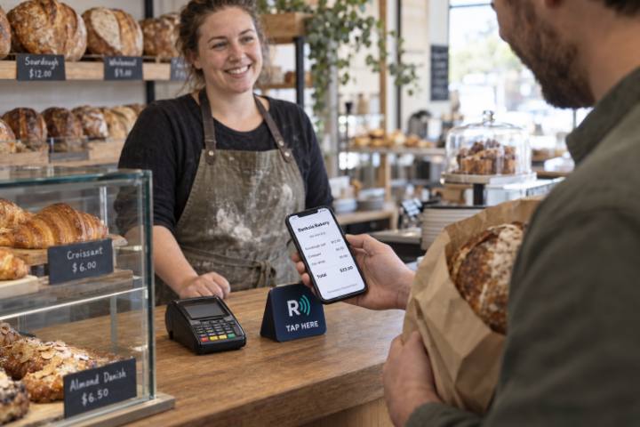 A customer with a bread bag views his ReceiptWave receipt at a bakery counter
